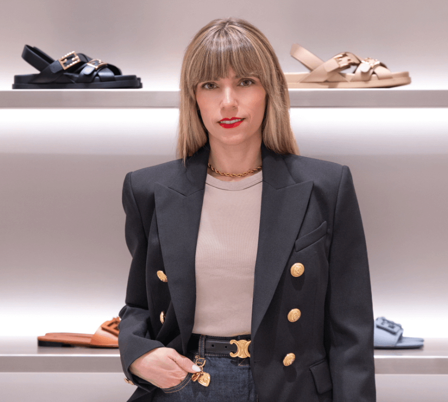 Raquel Macias standing confidently in a luxury boutique, wearing a tailored blazer with gold buttons, showcasing her polished and modern personal style.