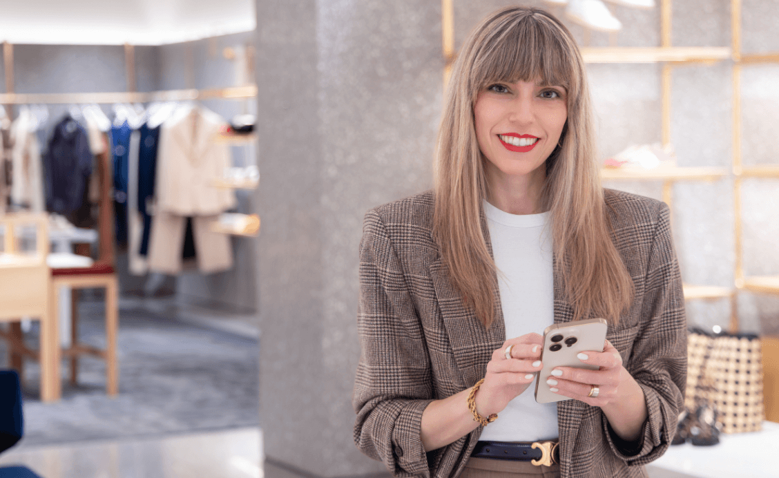 Raquel Macias smiling while holding her phone in a luxury retail setting, showcasing her polished and professional personal styling approach.